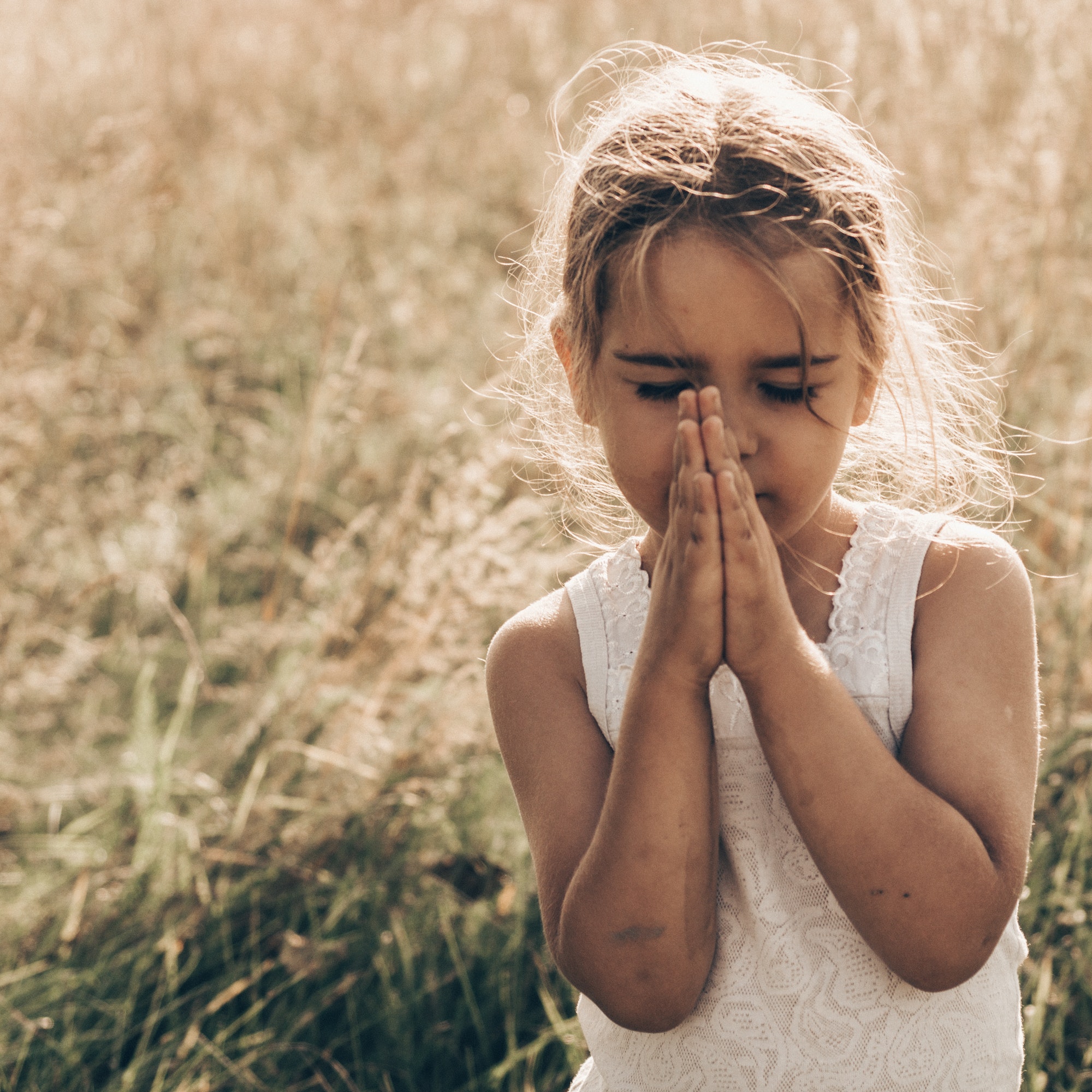 A child with hands folded in prayer in a field
